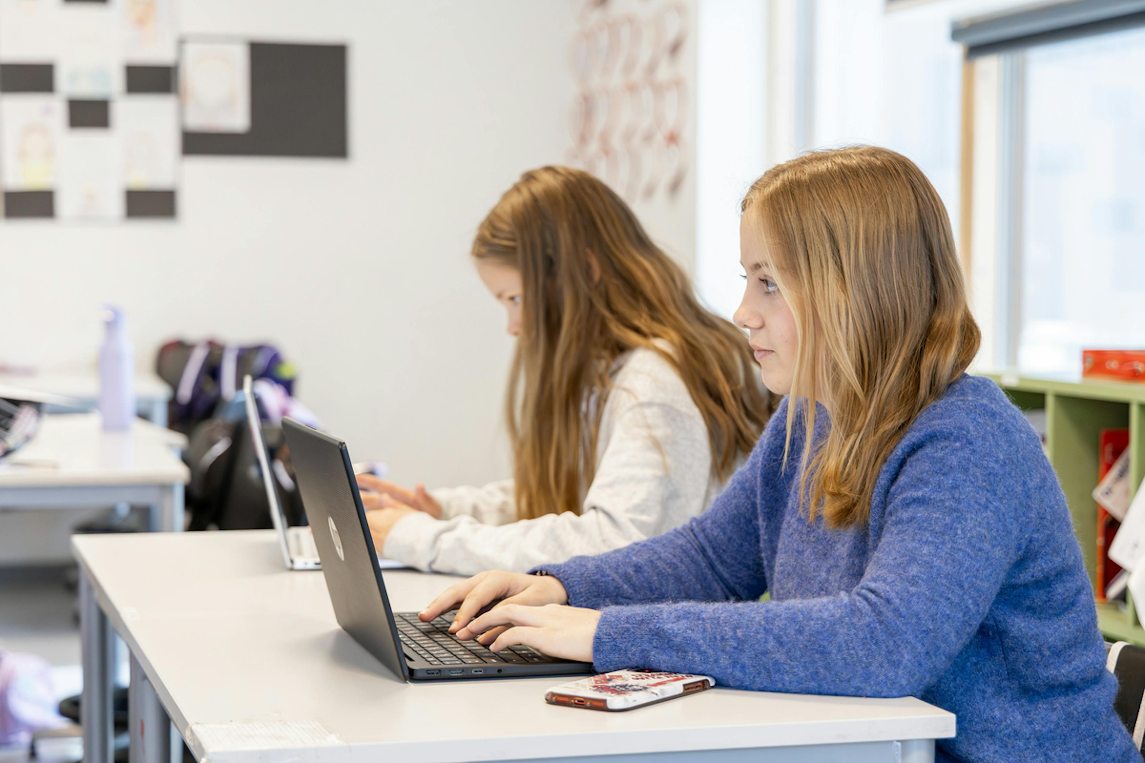 To studenter sitter i et klasserom med bærbare datamaskiner