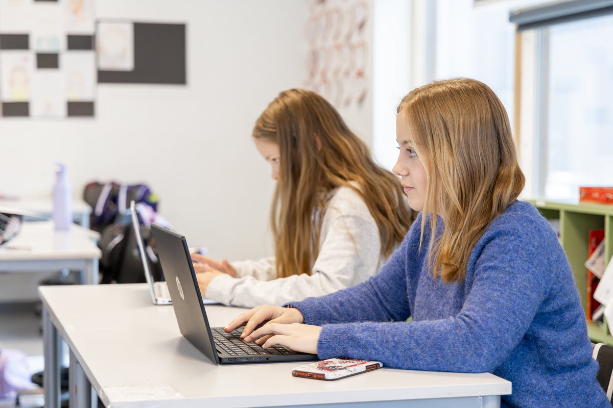 To studenter sitter i et klasserom med bærbare datamaskiner