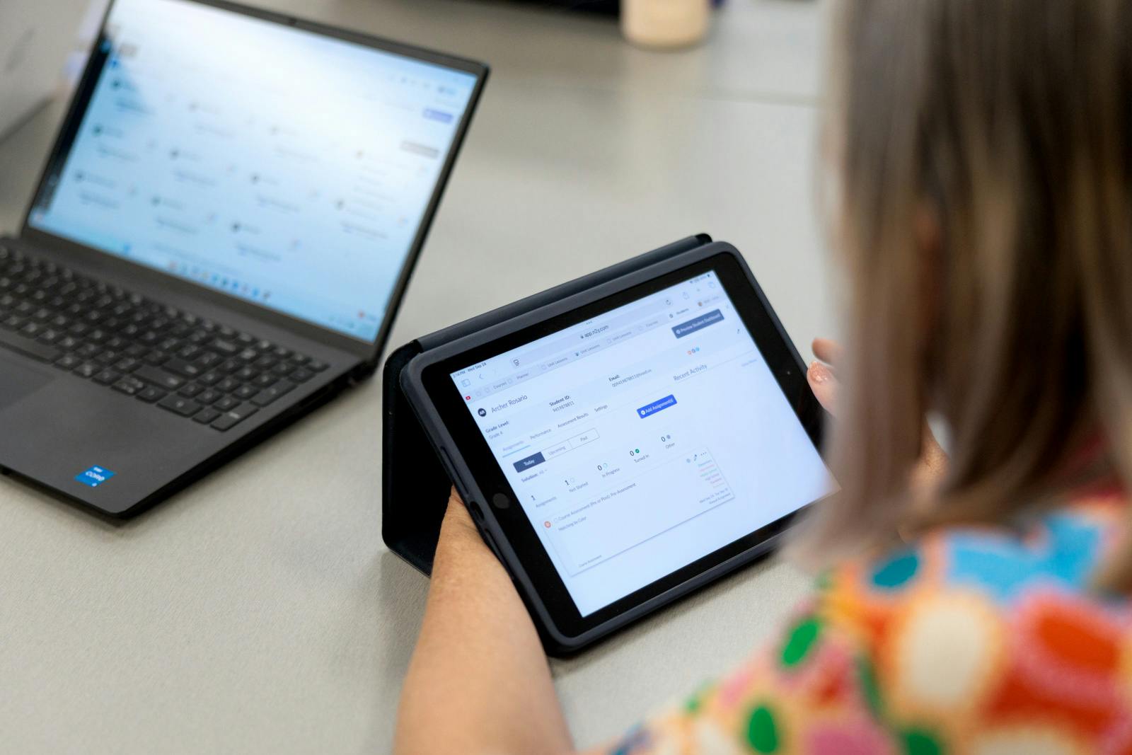 Person using a tablet displaying a digital dashboard, with a laptop open nearby during a training session.