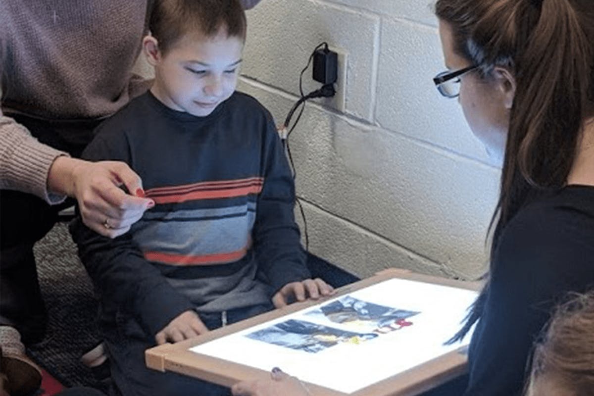 A young student uses a light box with the guidance of an instructor during a learning activity