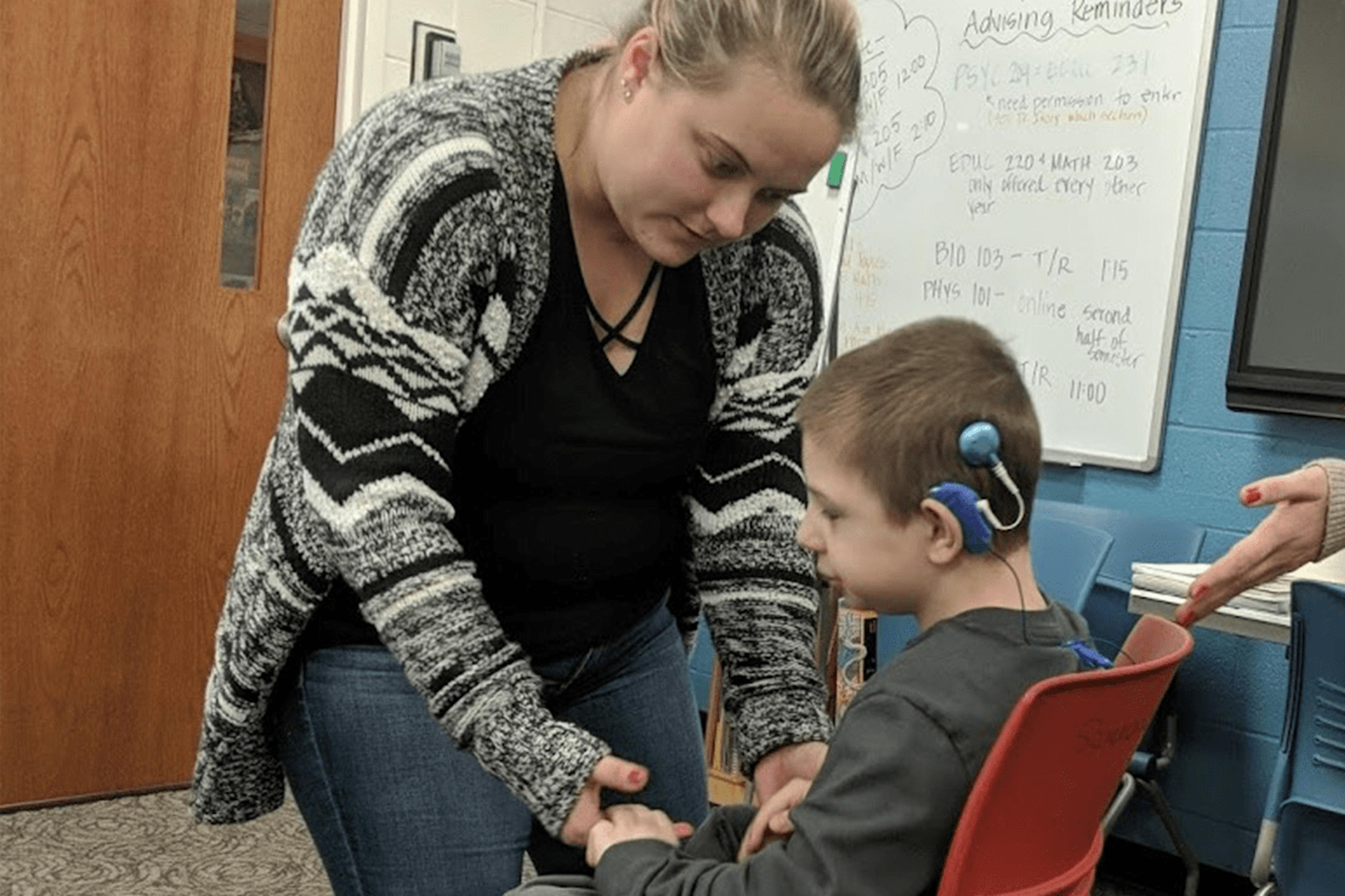 An educator assists a young student with cochlear implants during a classroom activity.