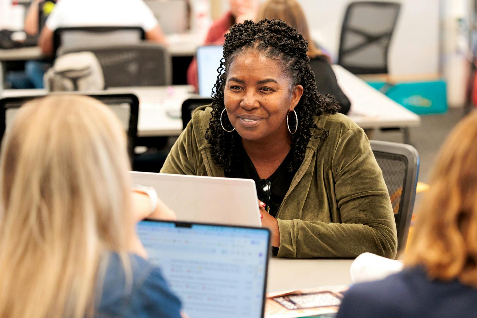 Woman smiling and speaking with two colleagues across laptops in a collaborative office setting