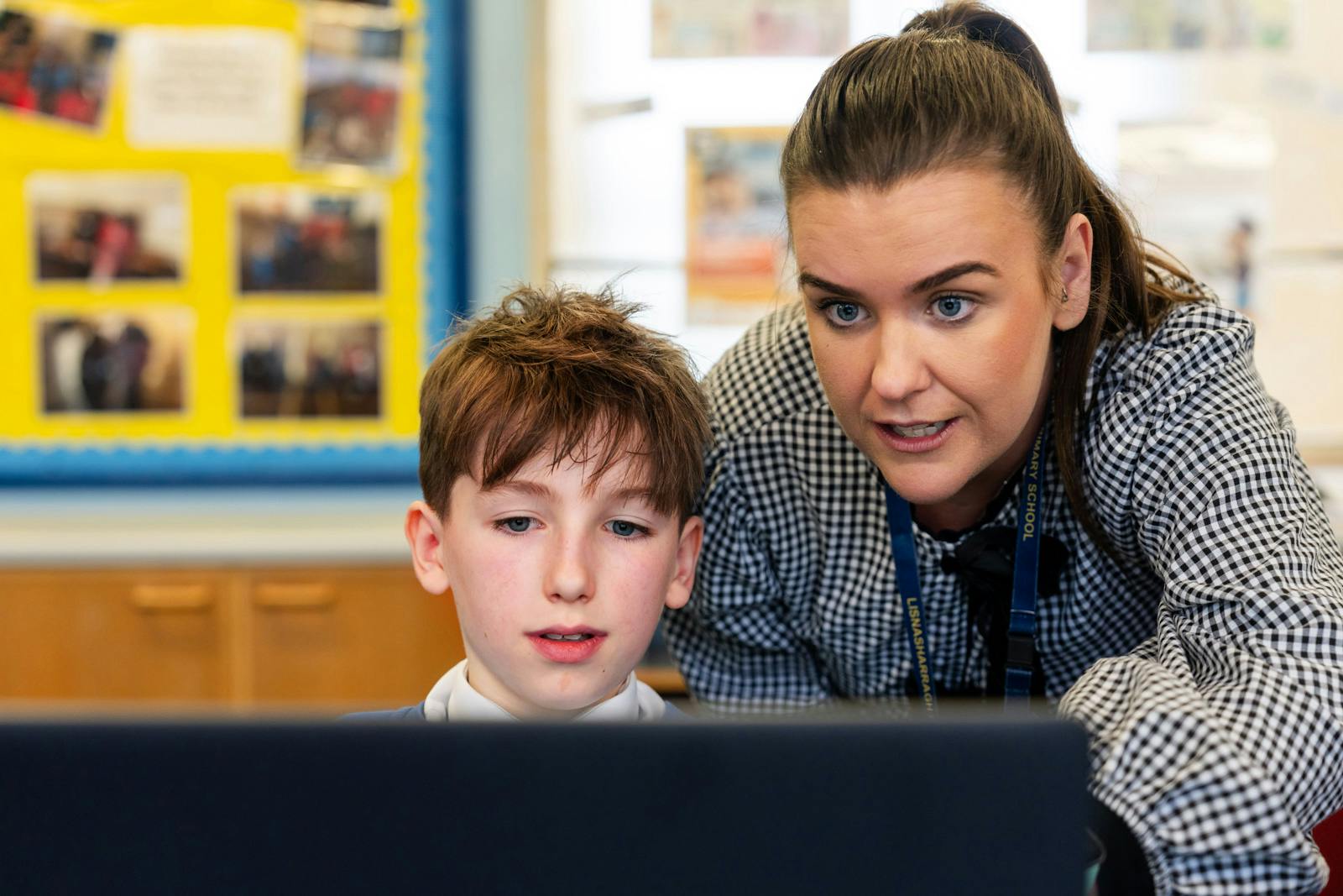 Teacher and student look intently at a laptop screen together in a classroom, focusing on a learning activity.