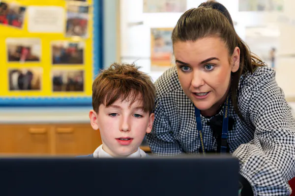 Teacher and student look intently at a laptop screen together in a classroom, focusing on a learning activity.