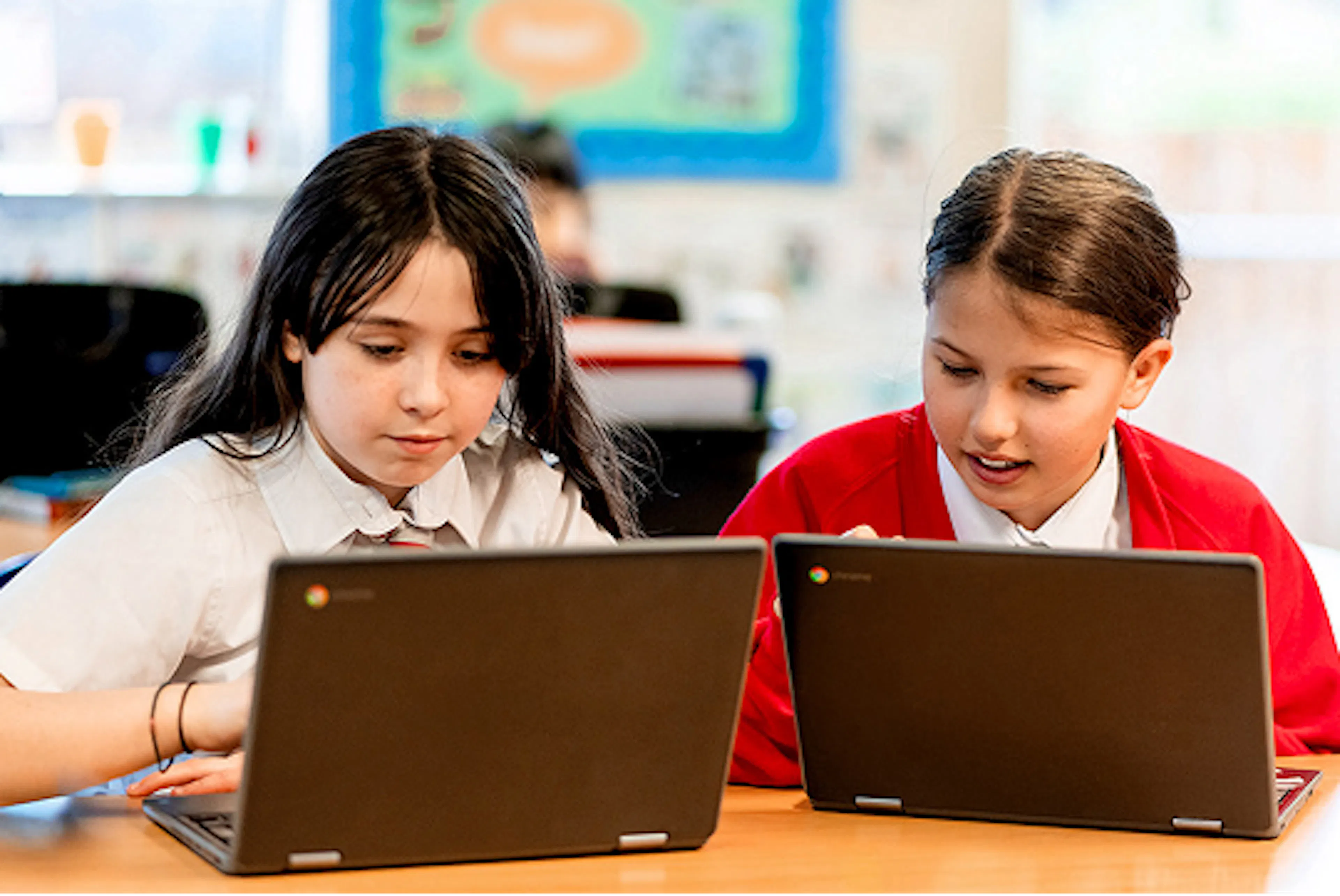 Two students using laptops together at a classroom desk, collaborating on a learning activity.