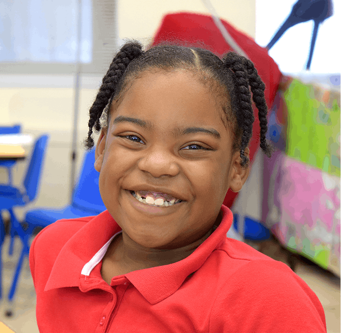 Smiling student in a red shirt sitting in a brightly colored classroom.