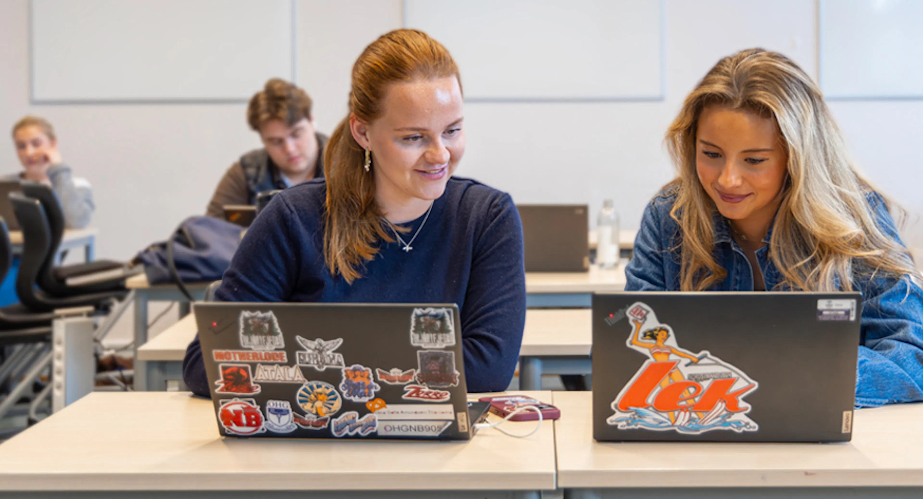 Students work at their computers in a modern classroom.