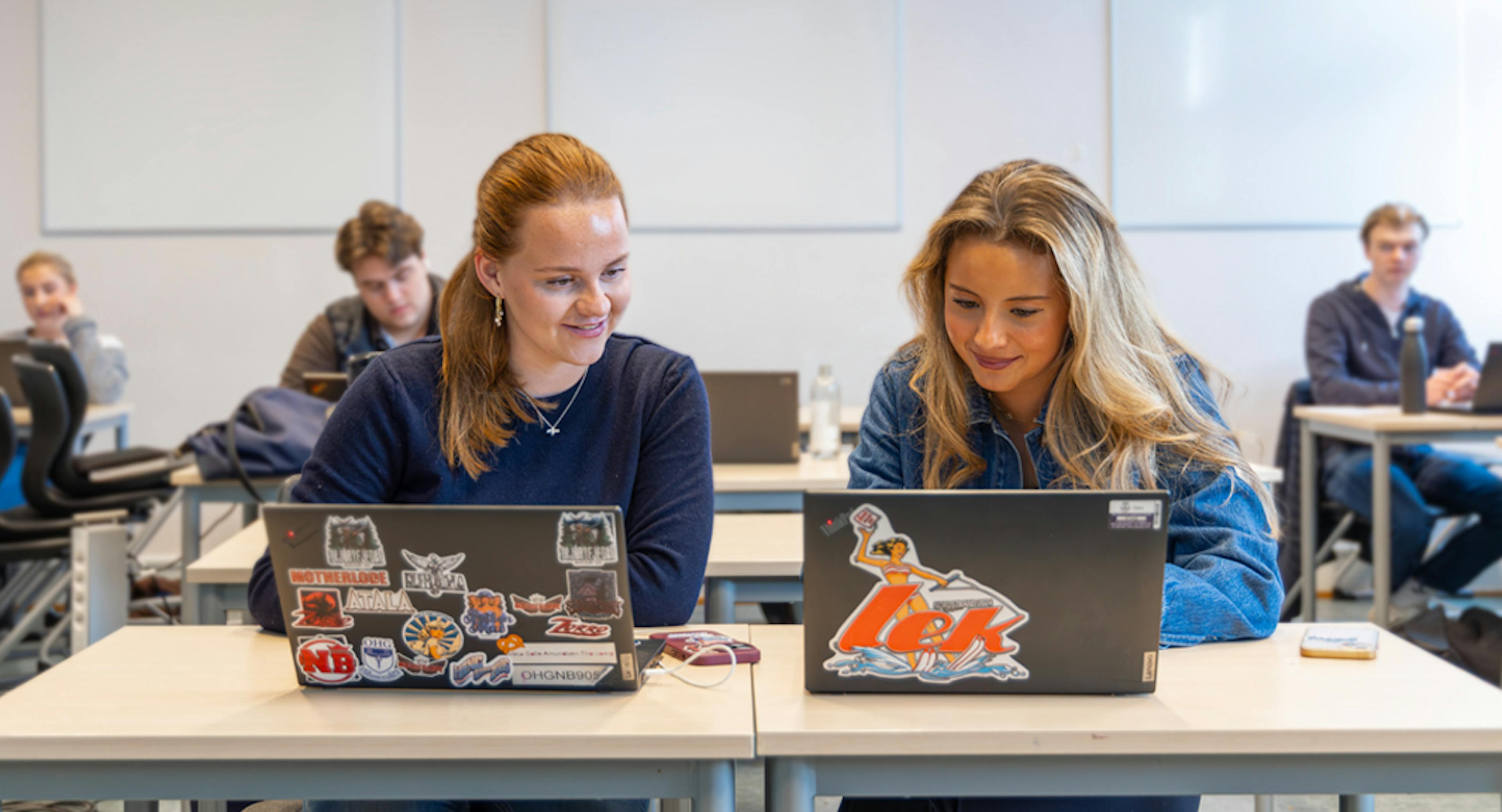 Studerende arbejder fokuseret ved deres computere i et moderne klasseværelse.