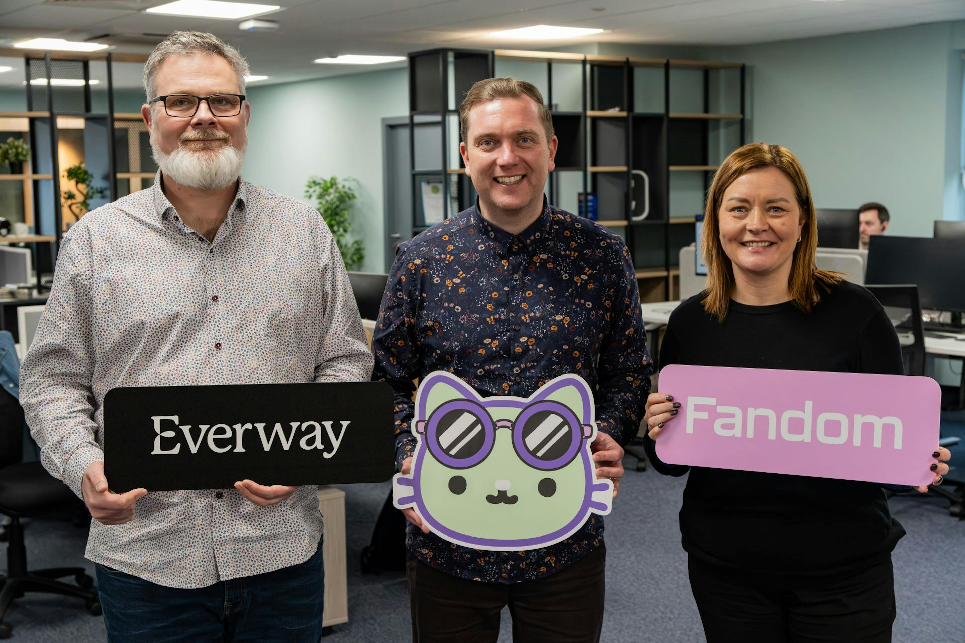 Everway software developer Matthew King, Sean Hanna from NOW Group and Everway's Chief People Officer Cathy Donnelly standing with Everway and Fandom branded signs in an office.