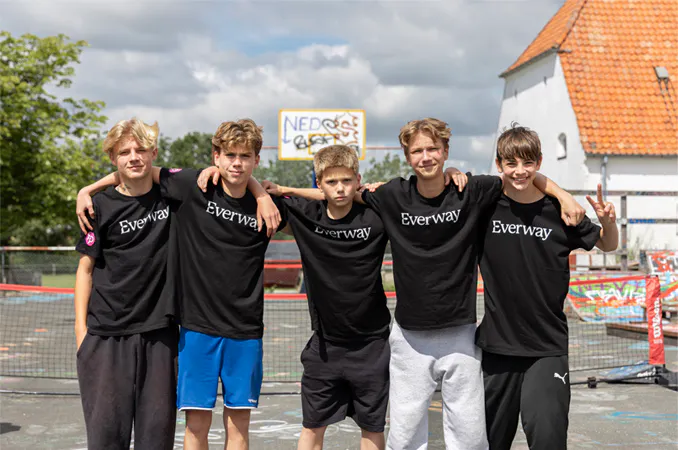 Fem drenge i Everway-T-shirts står arm i arm foran en udendørs bane.
