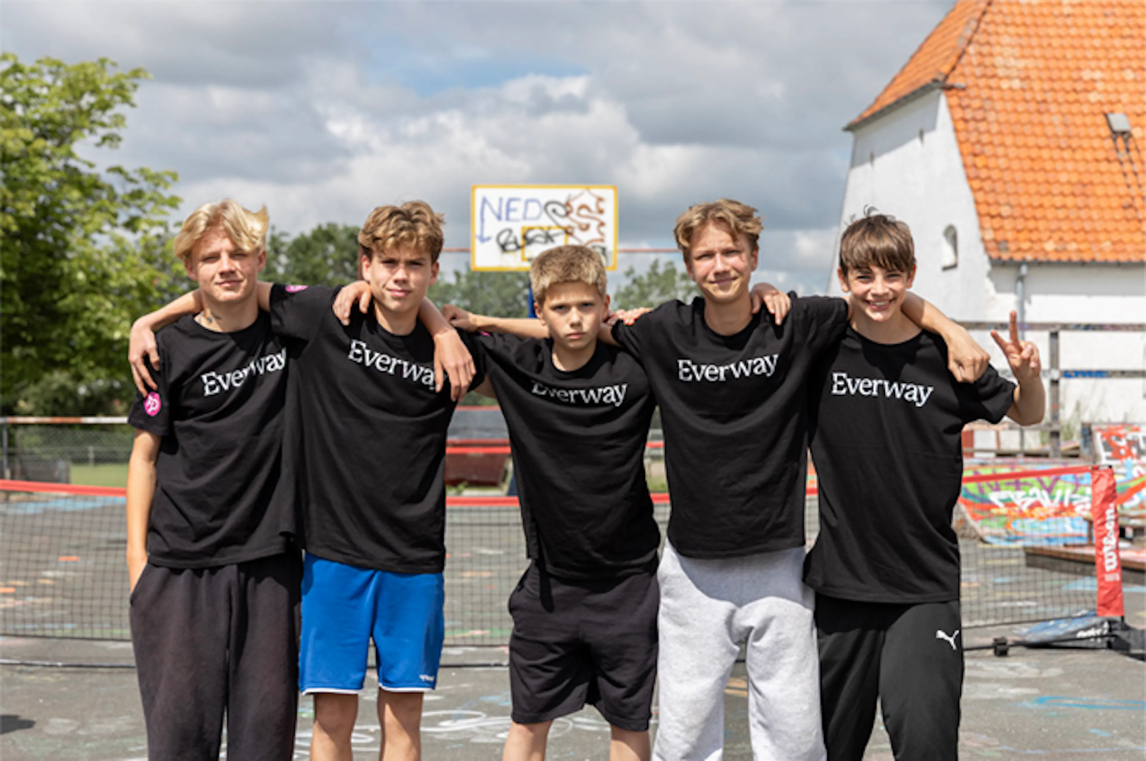 Fem drenge i Everway-T-shirts står arm i arm foran en udendørs bane.