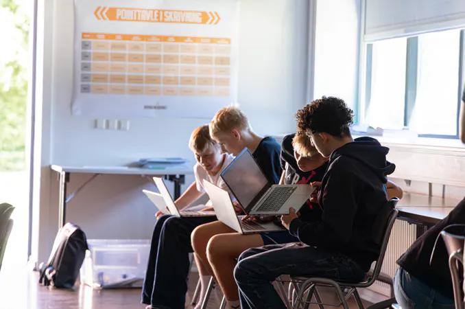 Fire unge arbejder sammen på bærbare computere i et undervisningslokale.