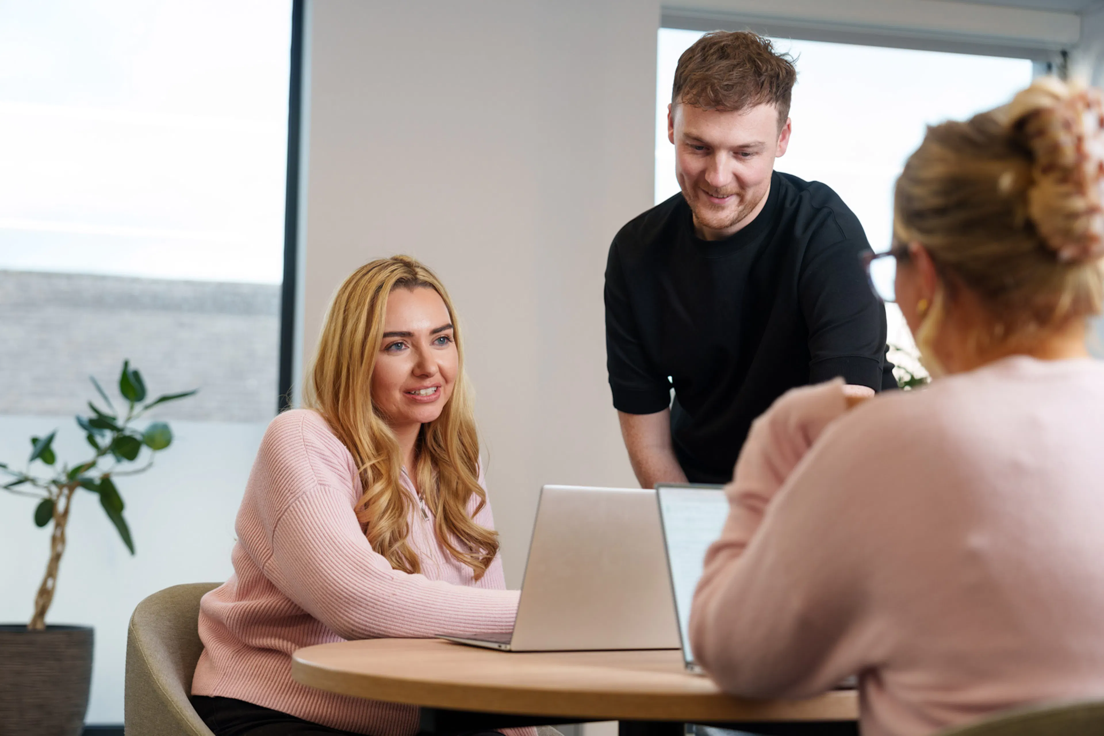 Three employees at a desk with laptops chatting