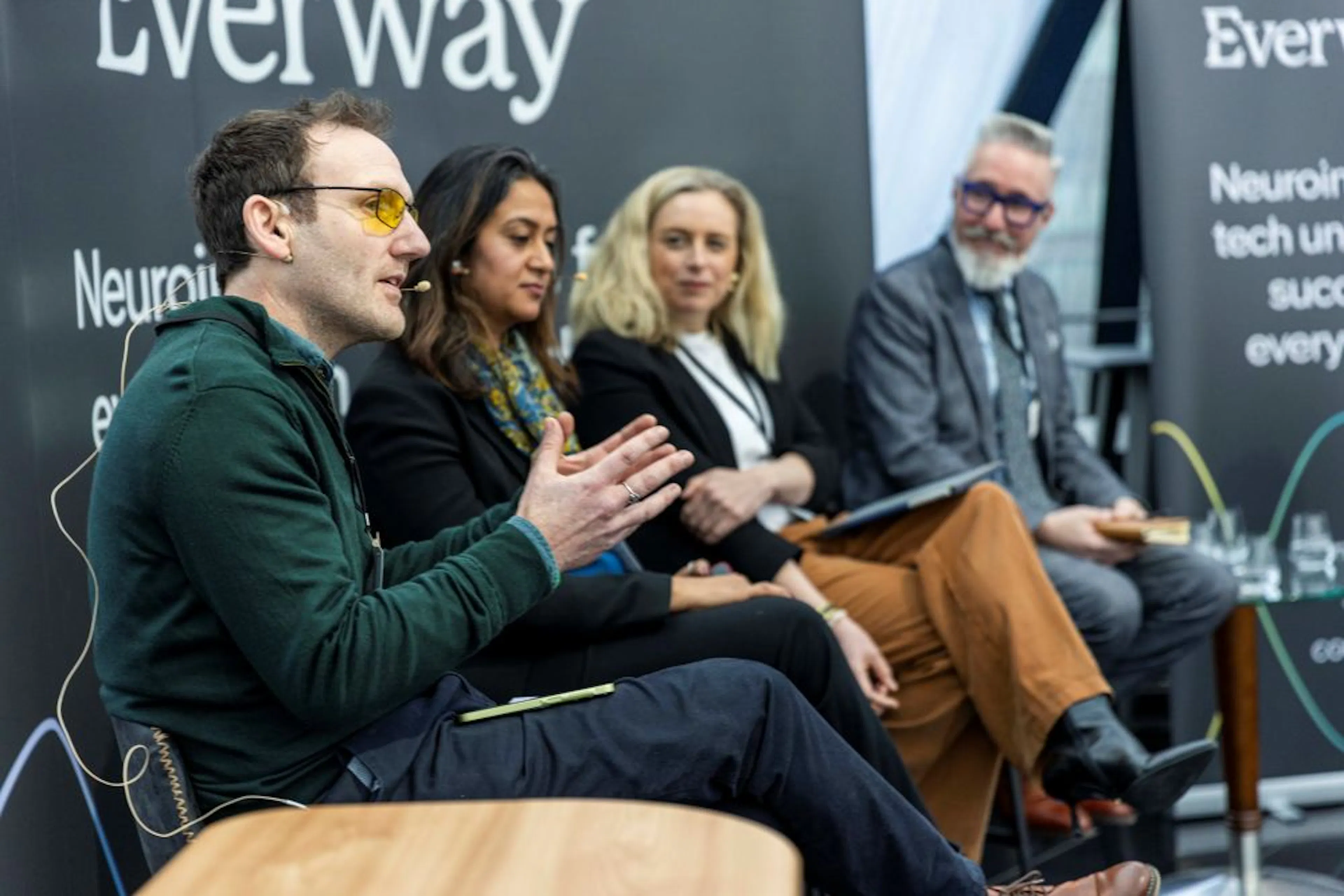 Four panelists on stage, one speaking.