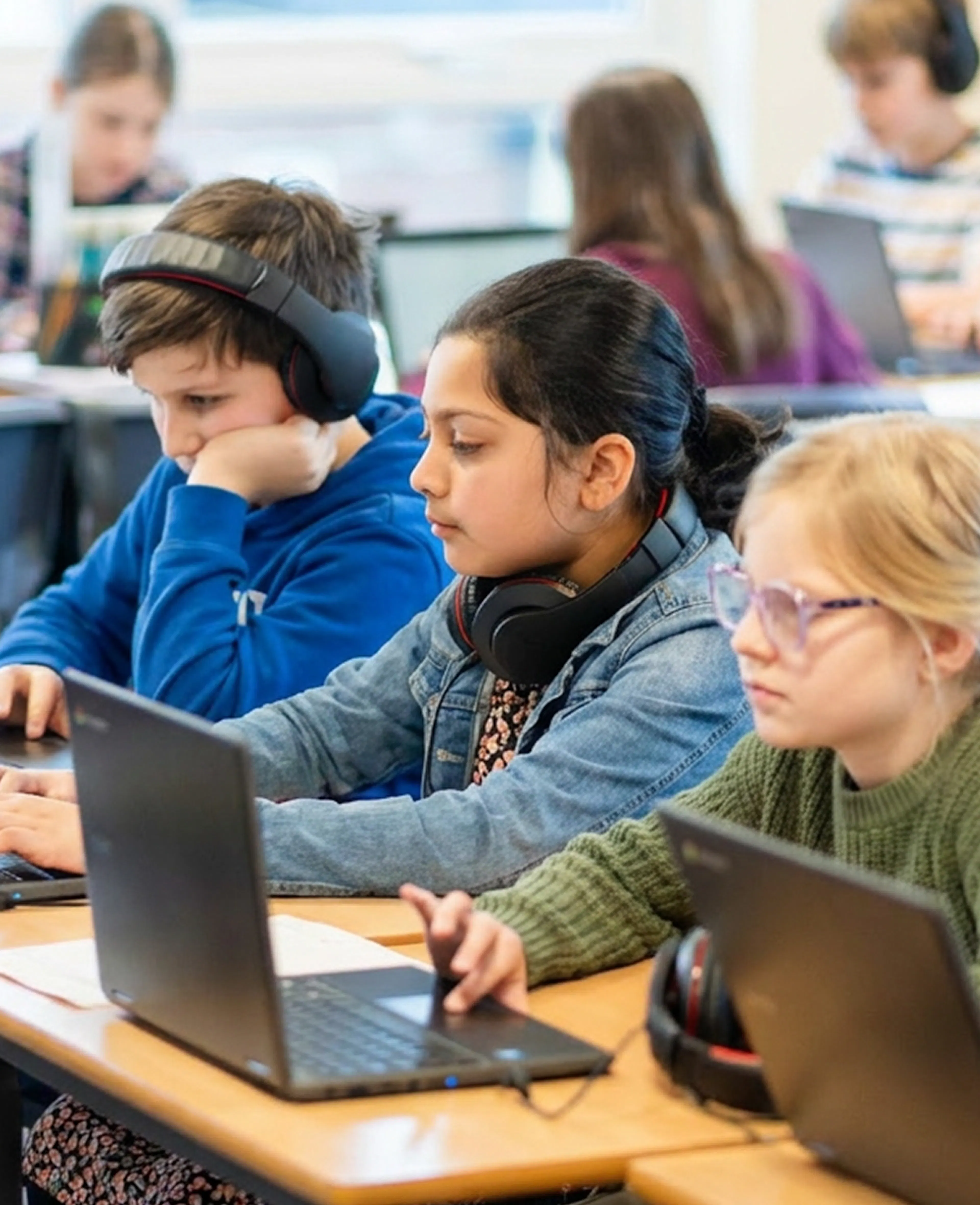 Students wearing headphones use laptops in a classroom while working independently.