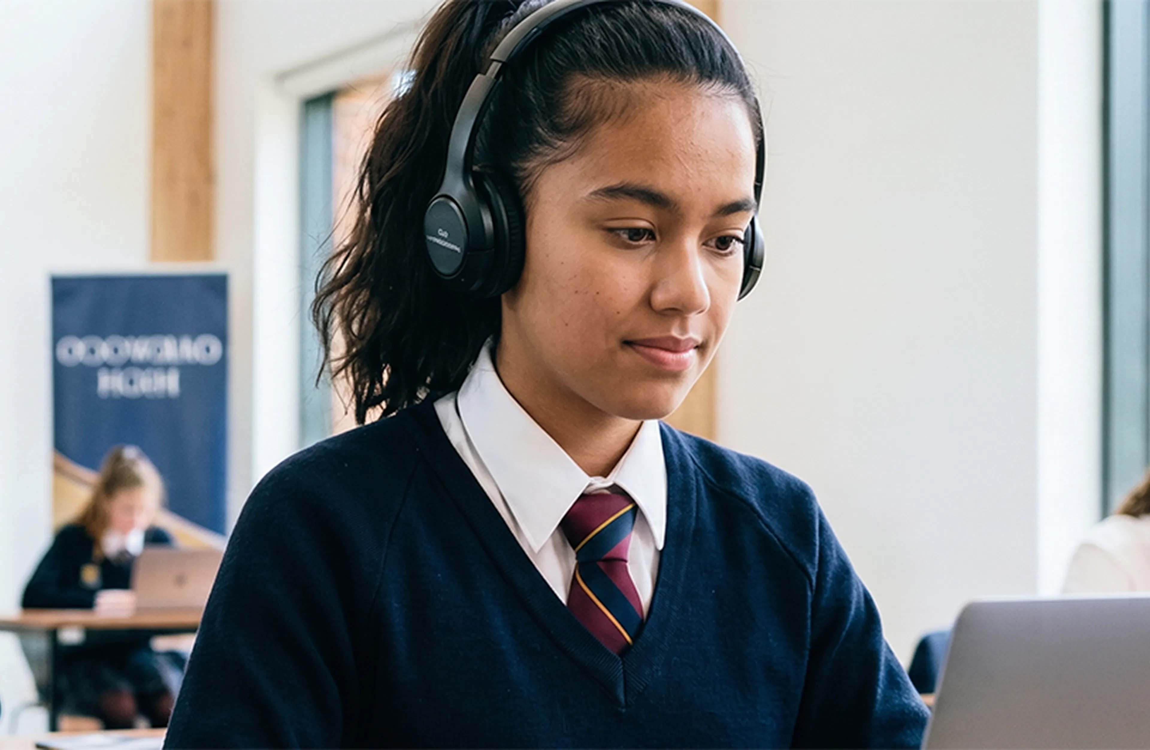Student wearing headphones uses a laptop during a classroom exam while other students work at desks.