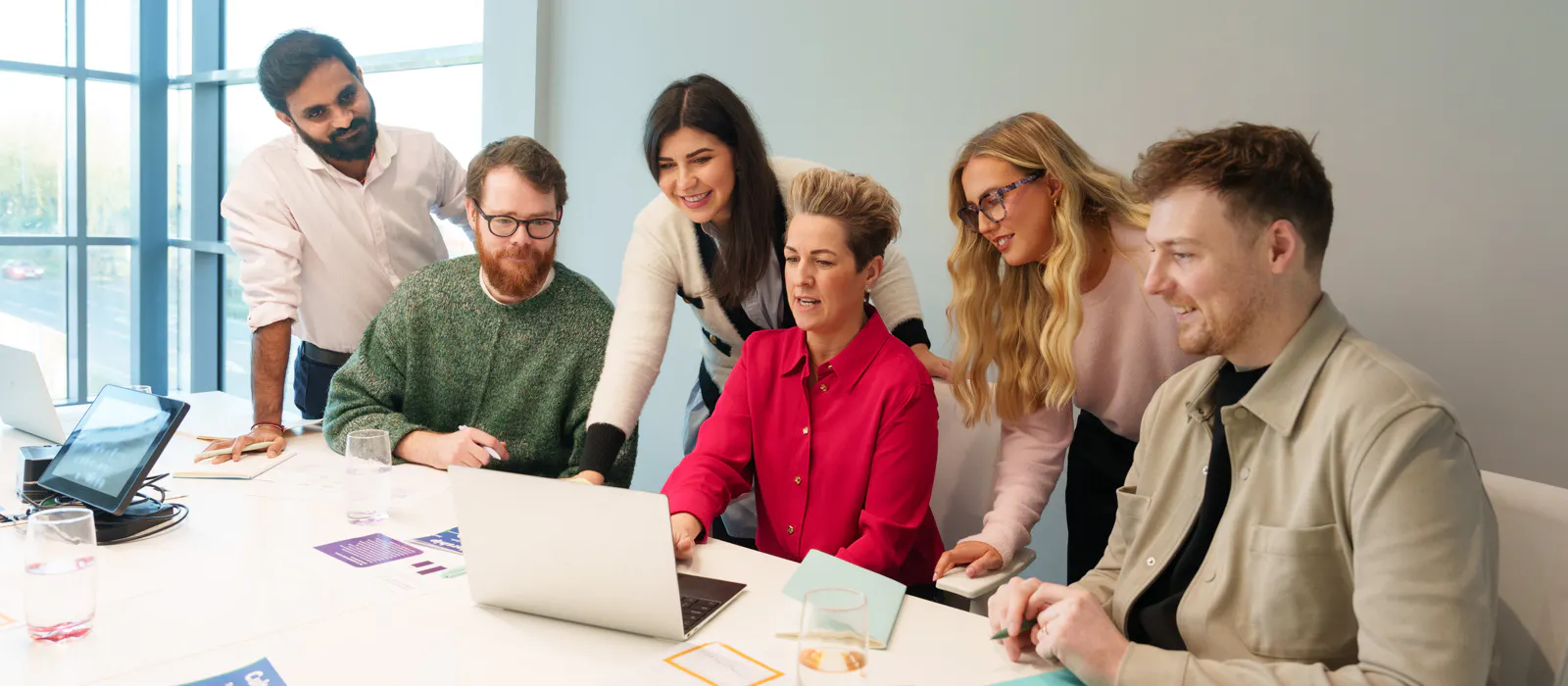 A team meeting around a desk. Everyone is looking at a laptop screen
