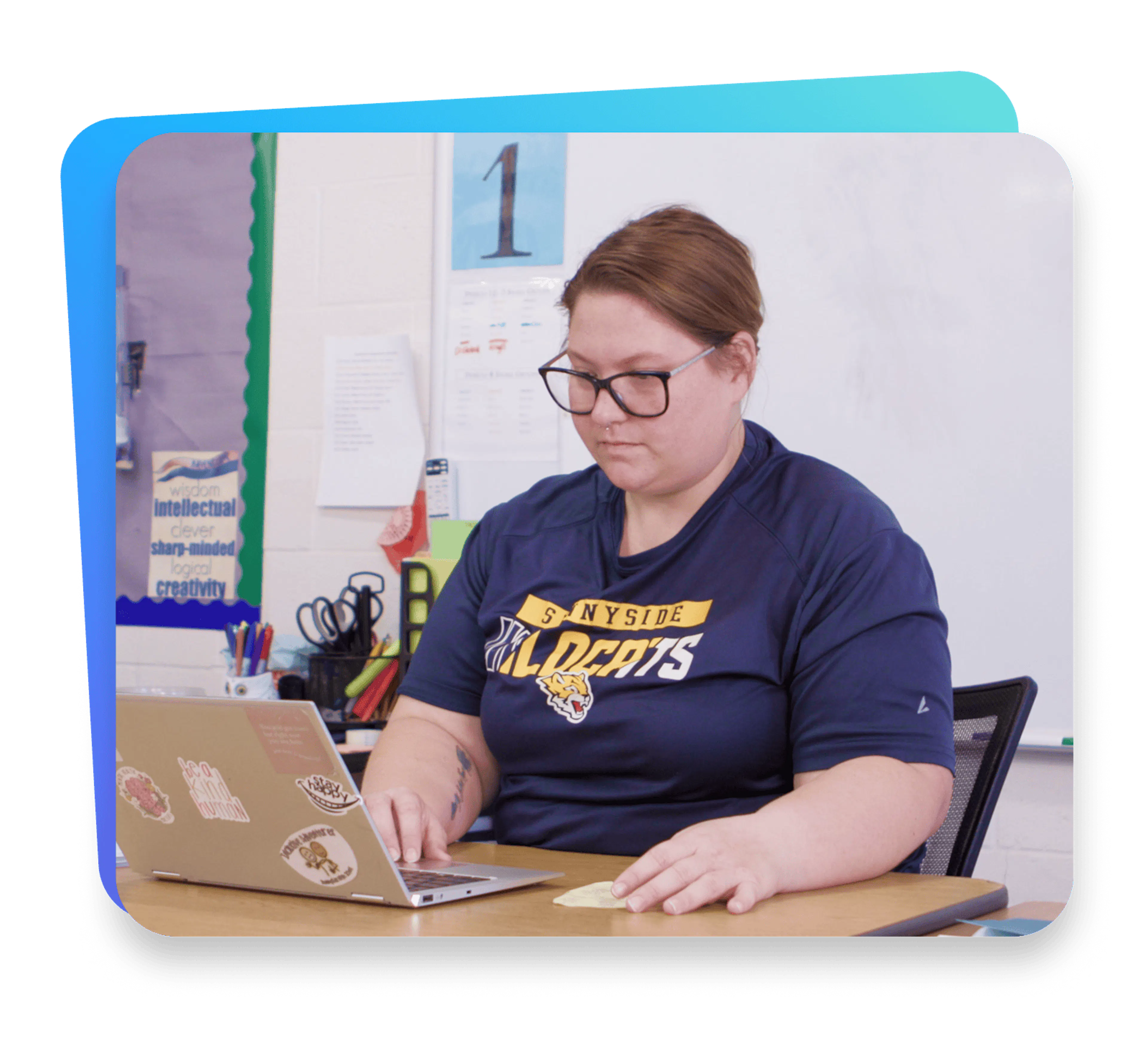 Teacher wearing glasses works on a laptop at a classroom desk, supporting digital IEP documentation and daily progress monitoring.
