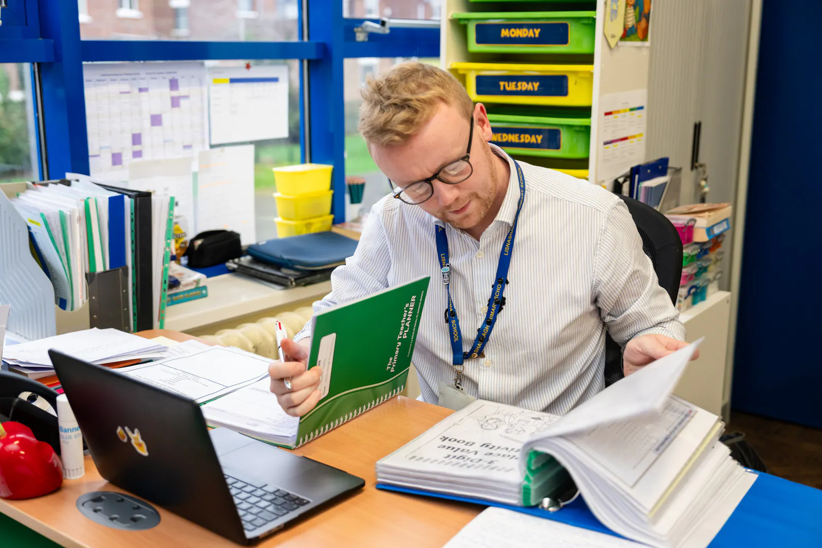 A teacher leafing through a file while sitting at a desk with a laptop