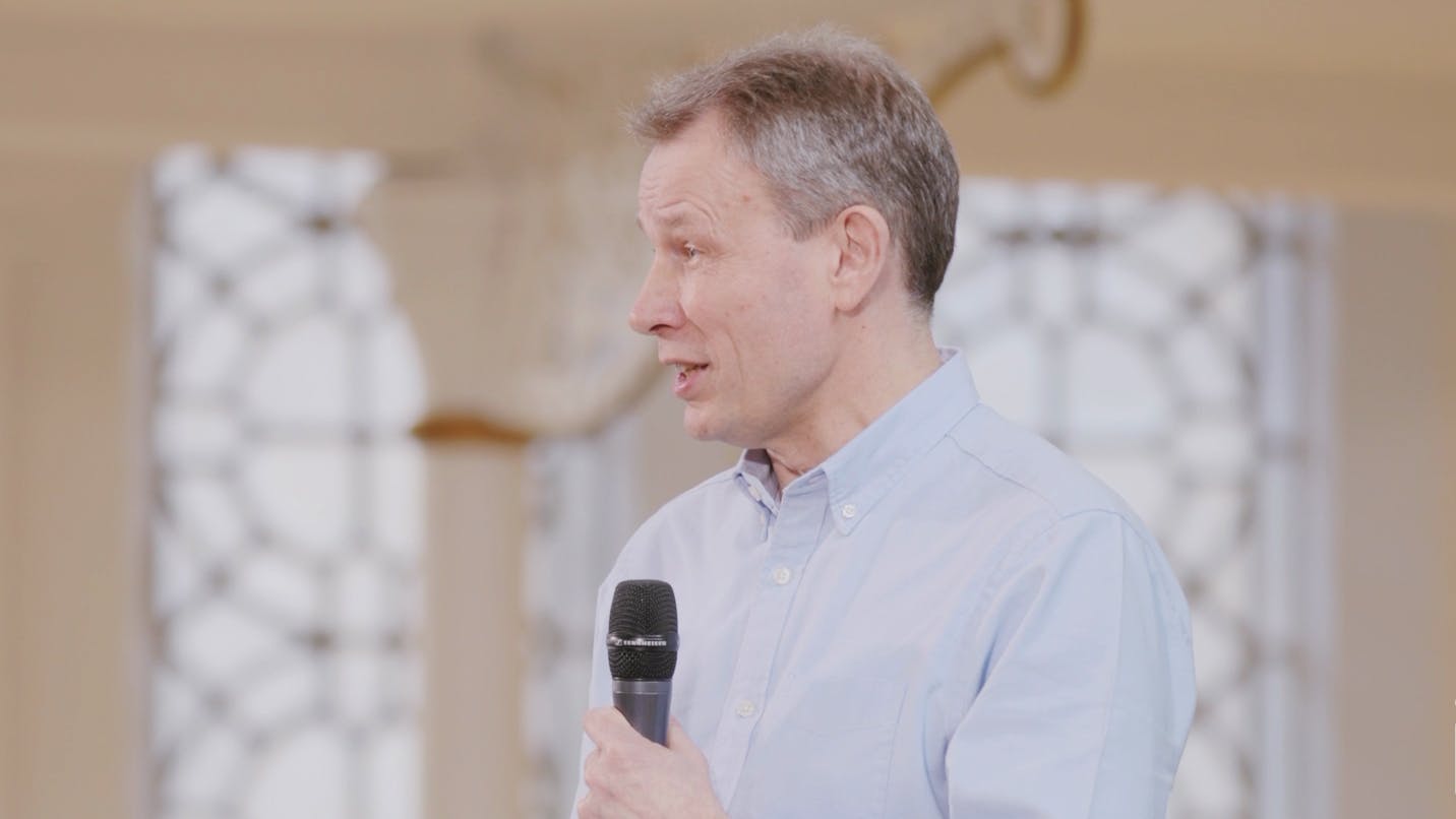 A screen capture of David Stroud's talk. He is holding his microphone to his chest and speaking to the audience.