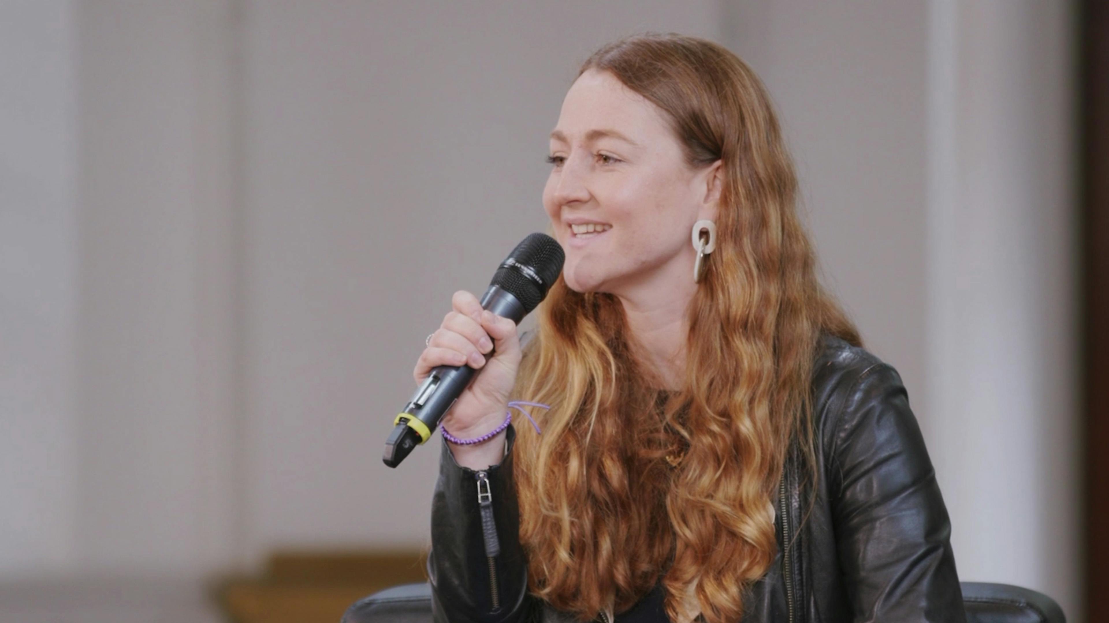 A screen capture of Caragh Bennet's interview. She is facing the audience and speaking into a microphone.