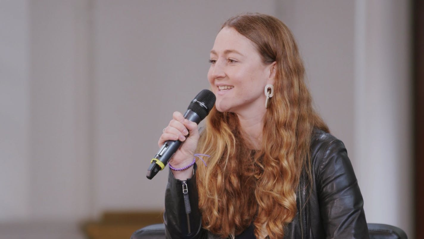 A screen capture of Caragh Bennet's interview. She is facing the audience and speaking into a microphone.