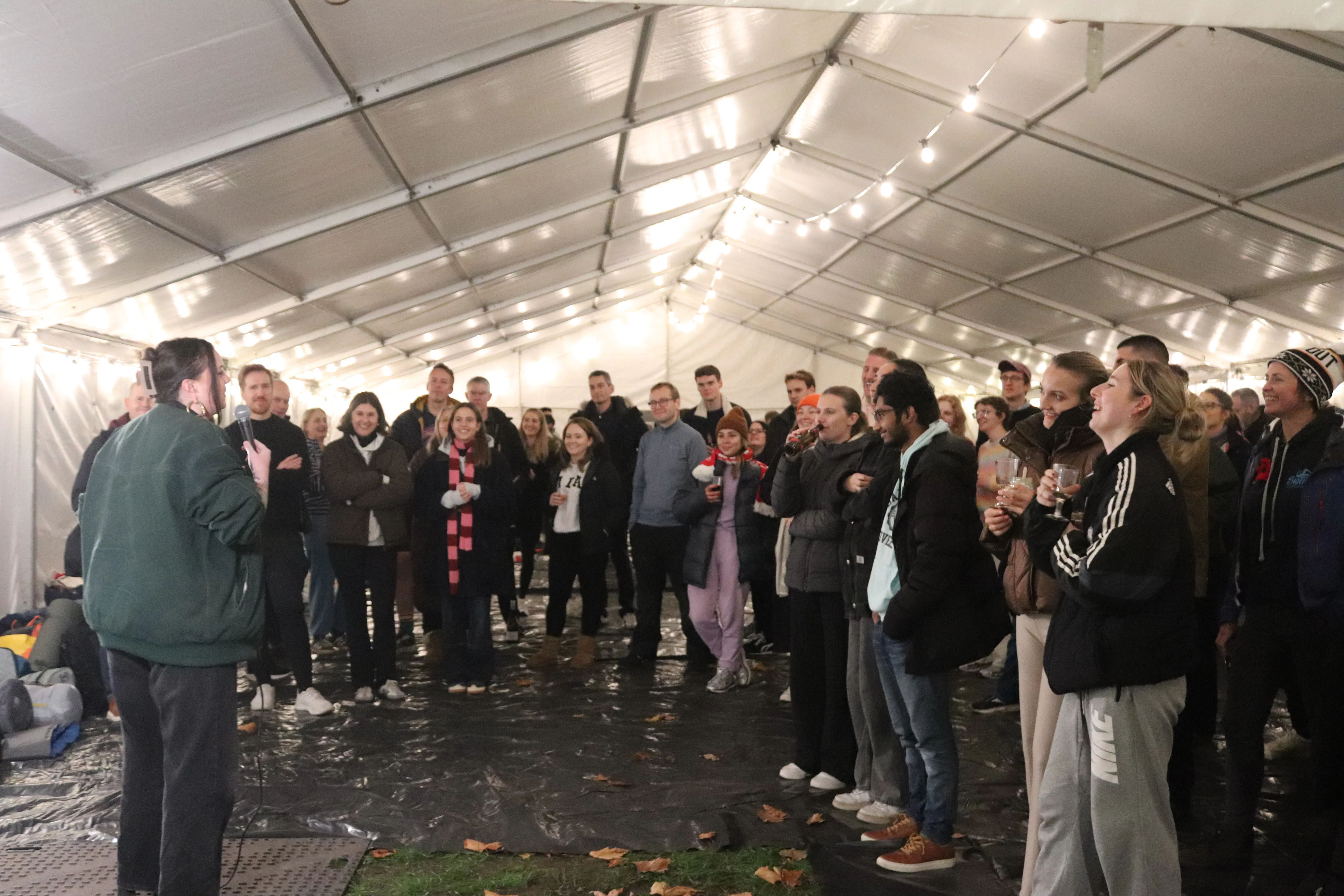 A group of participants listening to a speaker inside a lit marquee.