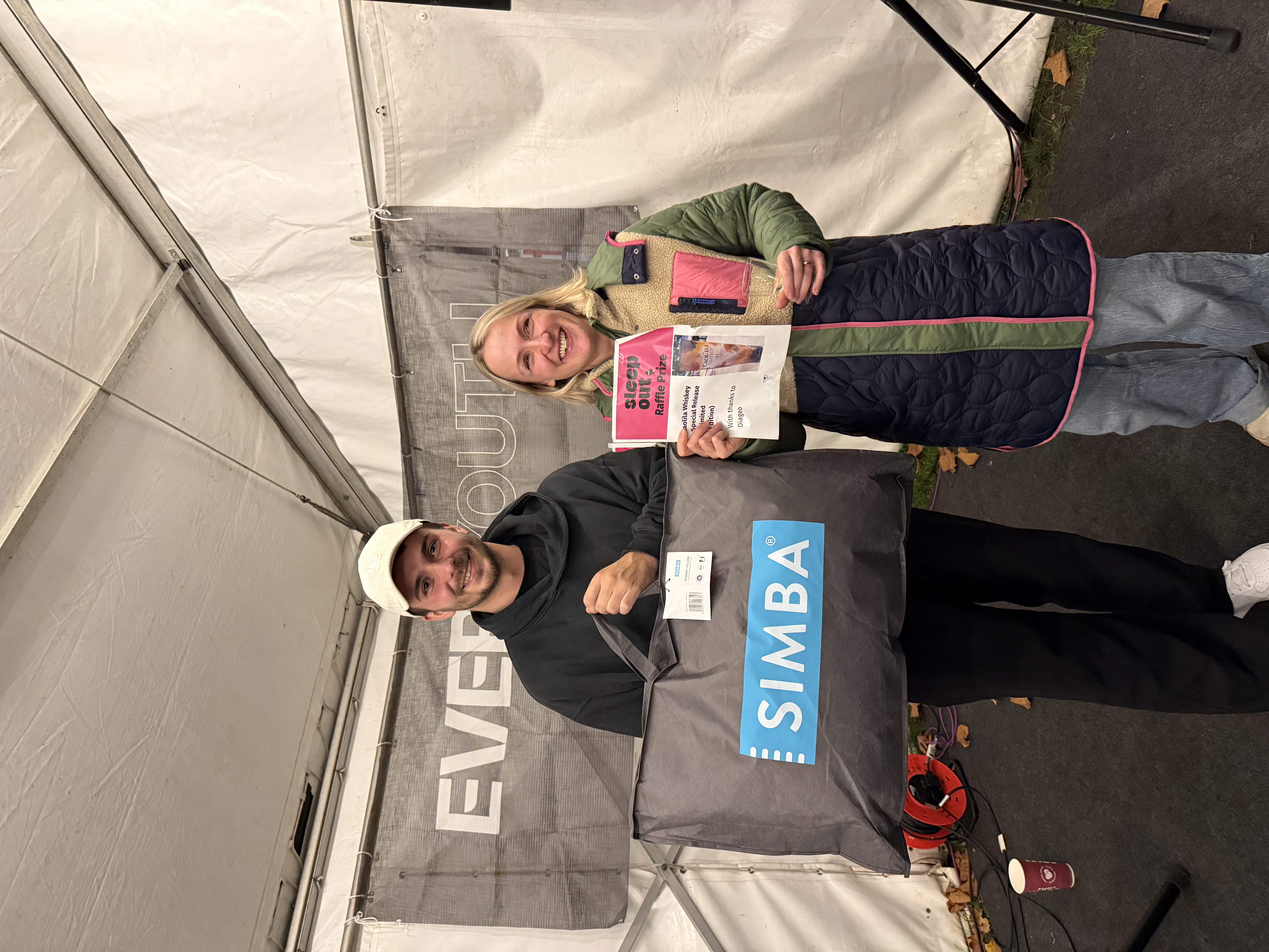 Two participants holding donation items and a welcome pack inside the event marquee.