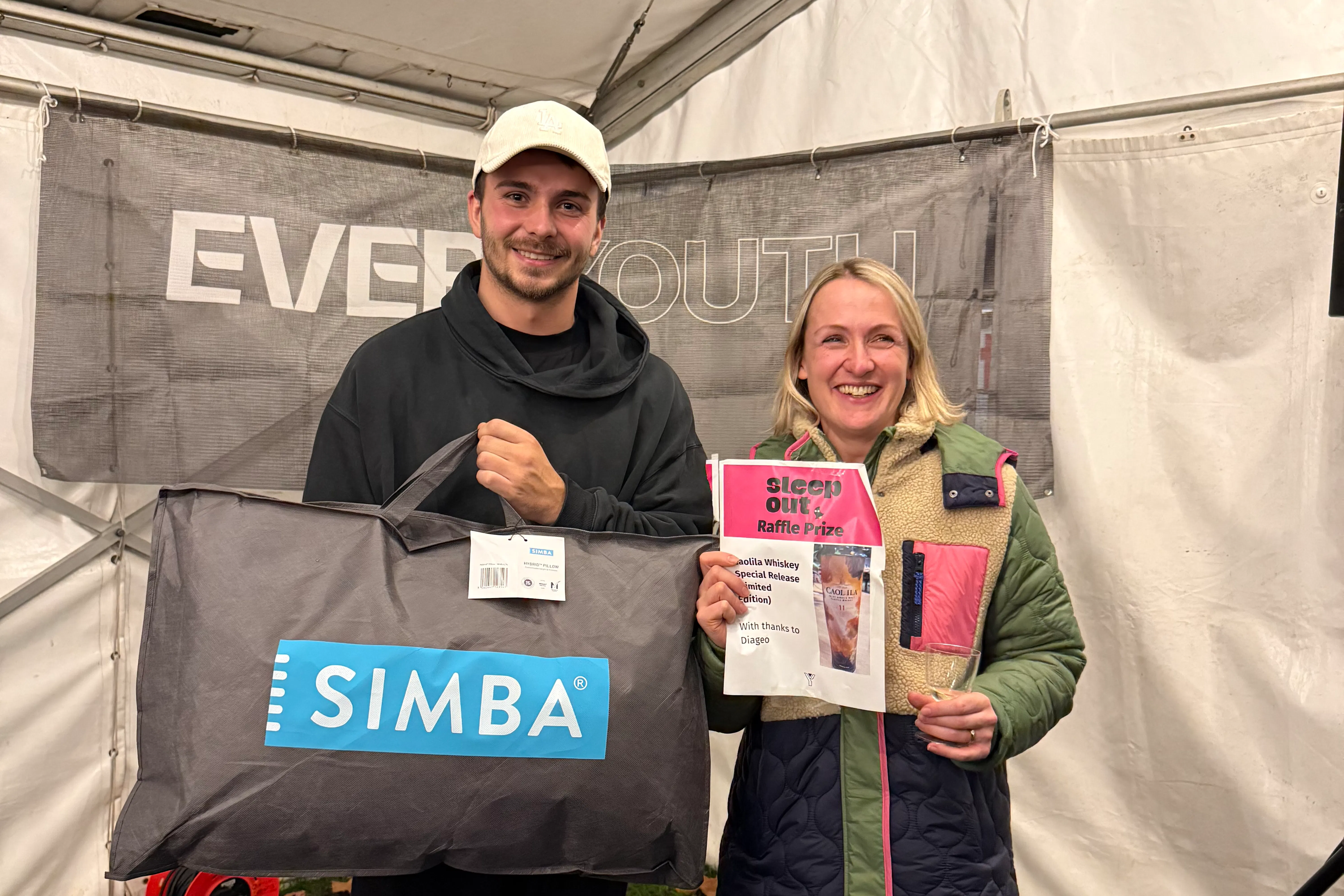 Two participants holding donation items and a welcome pack inside the event marquee.