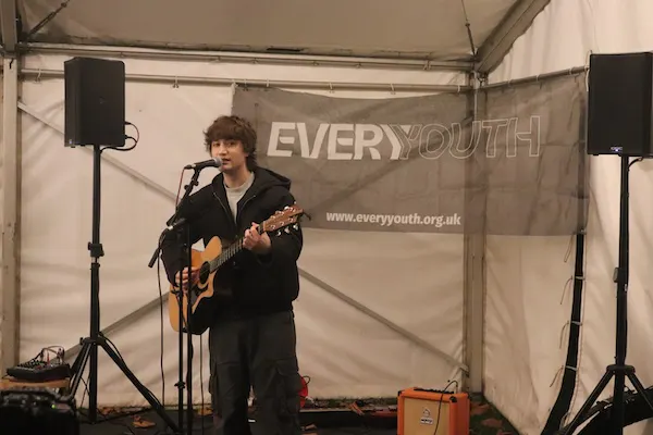 A musician performing with a guitar and microphone inside a marquee at the event.