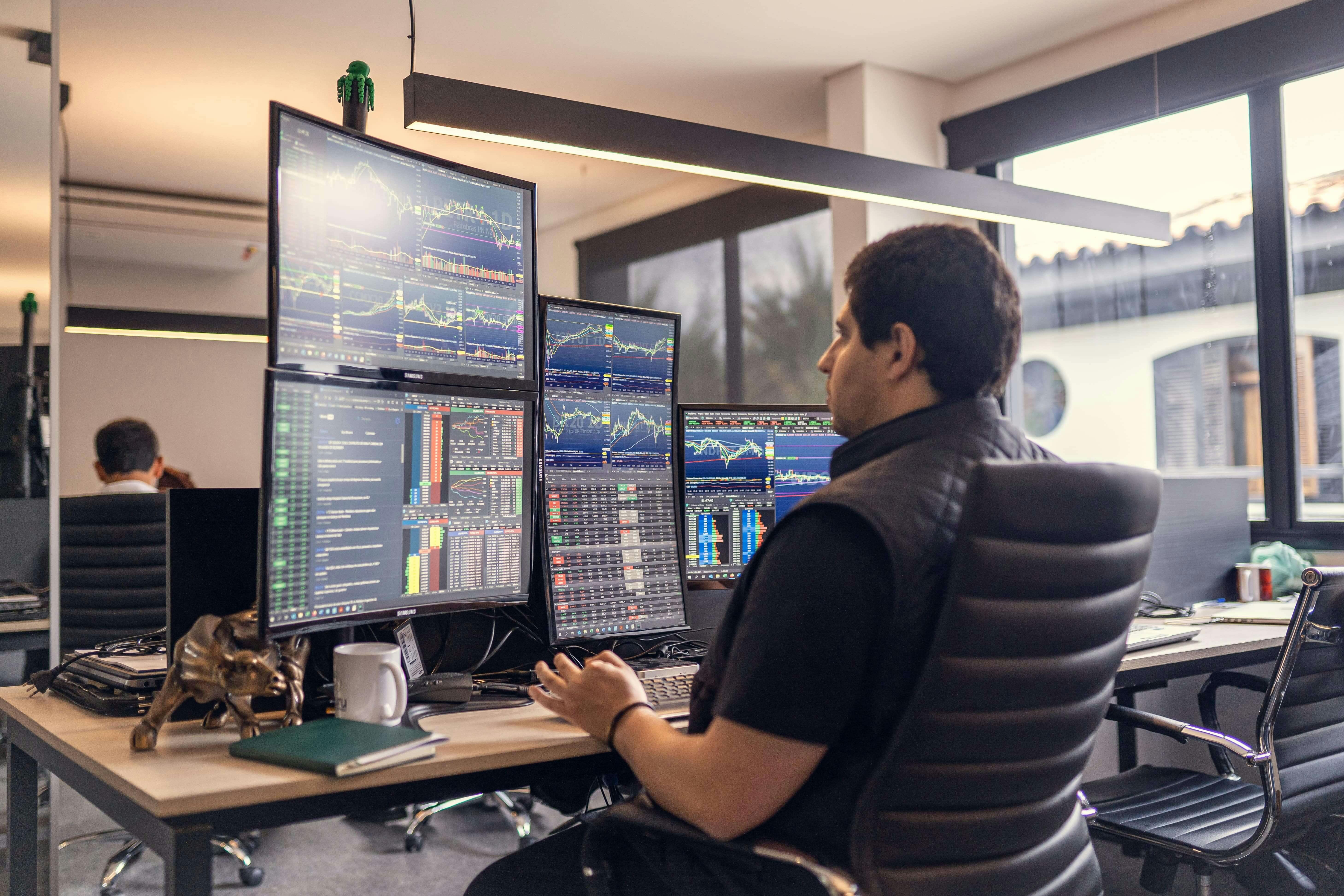 Rafael Bombini olhando para telas com gráficos do mercado de ações. 