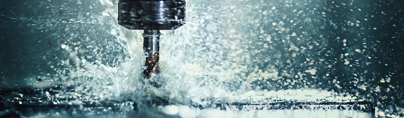 A close-up photo of metal being machined, with fluid splashing.