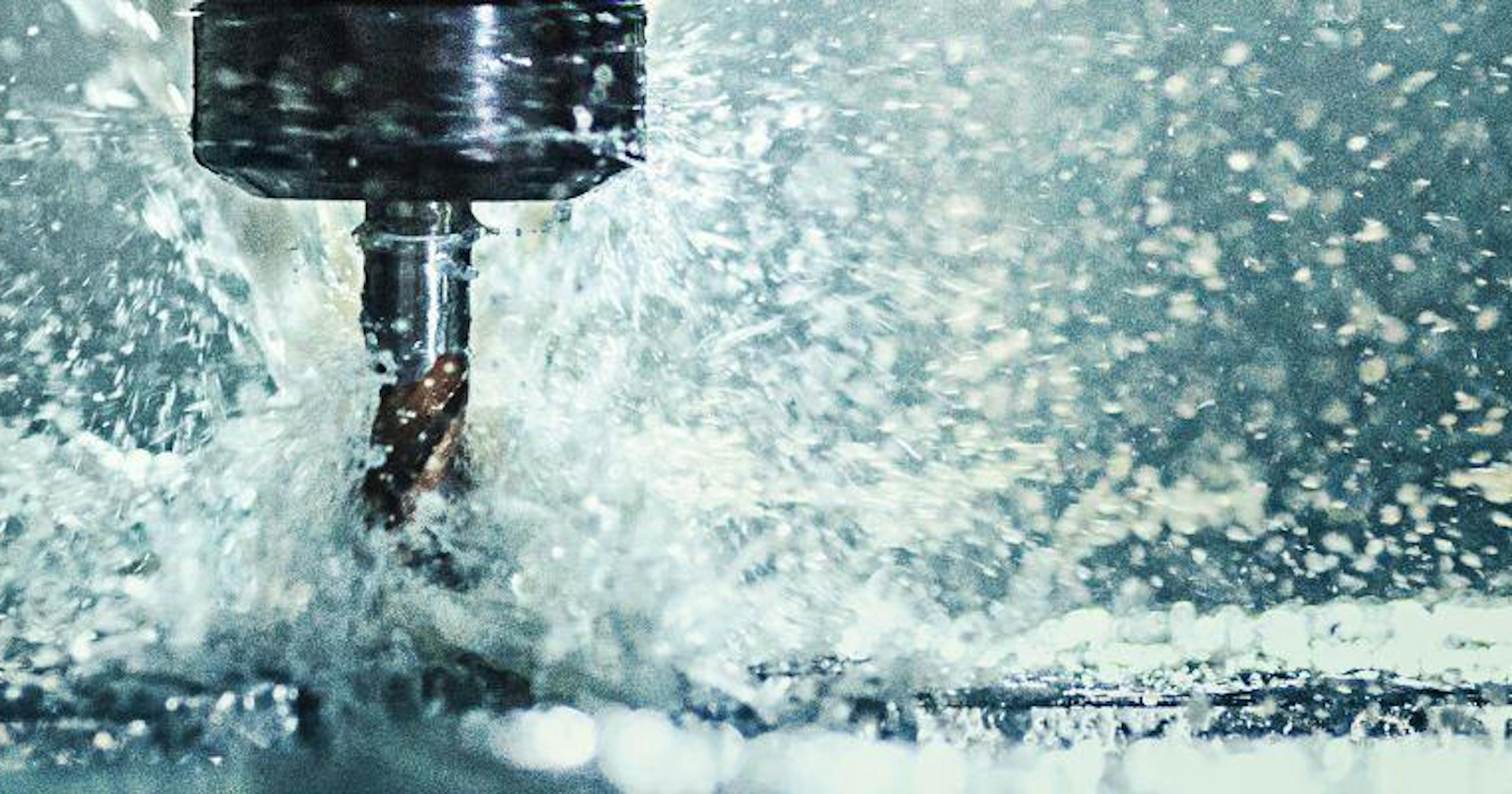 A close-up photo of metal being machined, with fluid splashing.