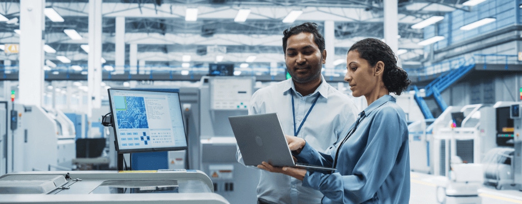 Engineers reviewing real-time industrial monitoring data on a laptop inside a manufacturing facility