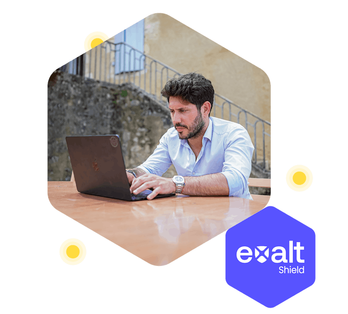A person working on their computer, with the Exalt Shield logo beside them.