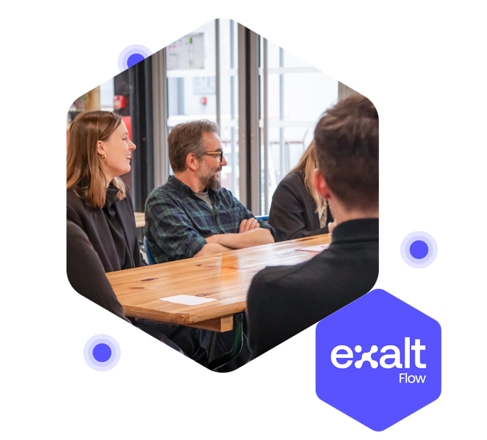 Several people sitting around a table, attending a meeting, with the eXalt Flow logo beside them.
