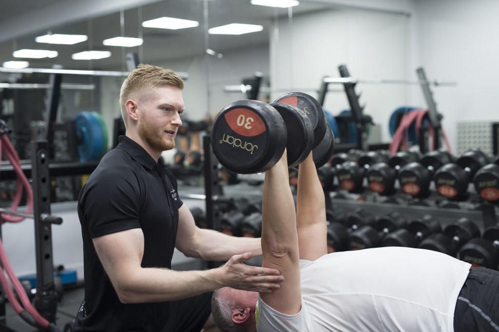 A client being helping using dumbbells by an Exclusive Fitness Trainer