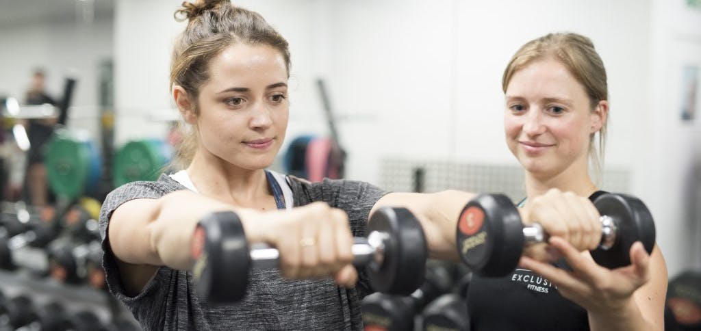 An Exclusive Fitness Trainer helping guide a client while using dumbbells