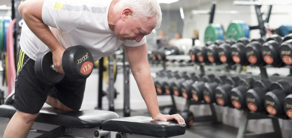 Man bent over a bench, pulling a dumbbell to his chest.