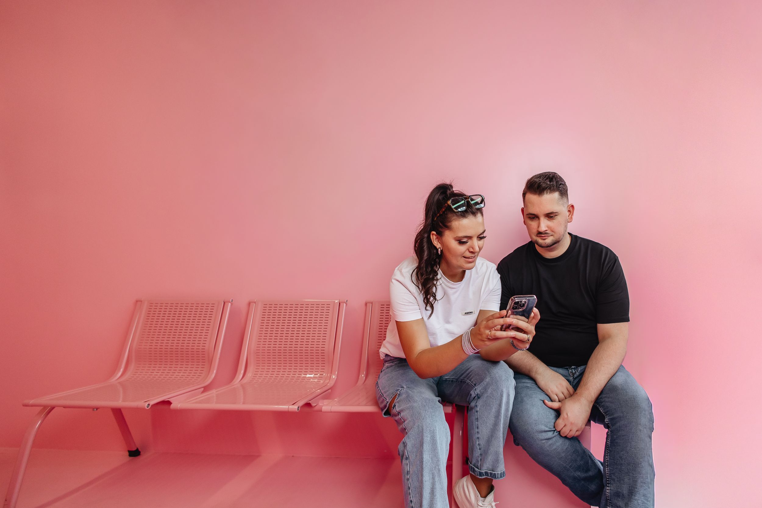 Zwei Mitarbeiter der Social Media Agentur Exportarts auf einer pinken Bank schauen auf ein iPhone