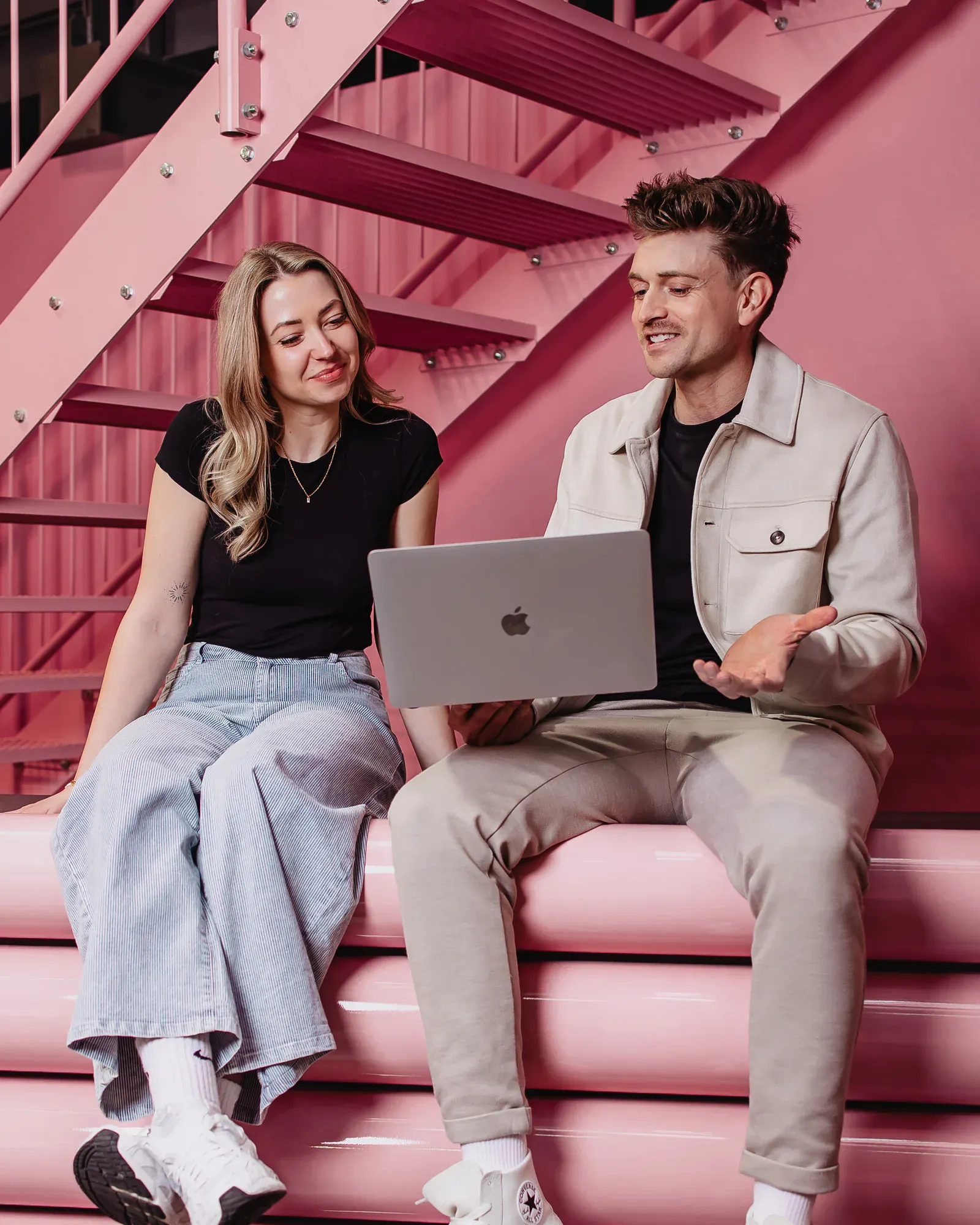 Zwei Mitarbeiter der Online Marketing Agentur Exportarts sitzen mit einem Macbook auf einer pinken Theke 