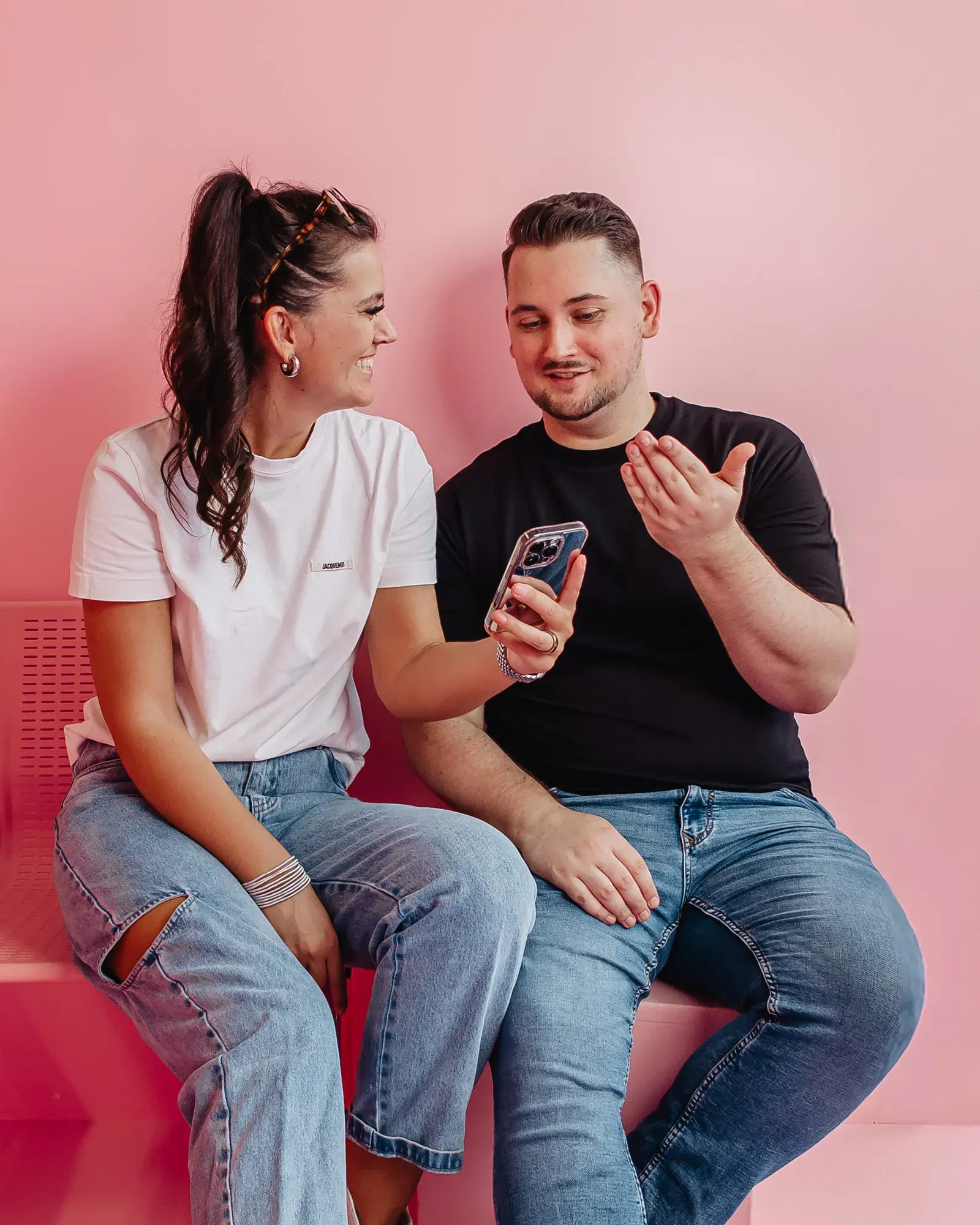 Zwei Personen sitzen mit einem iPhone auf einer pinken Bank