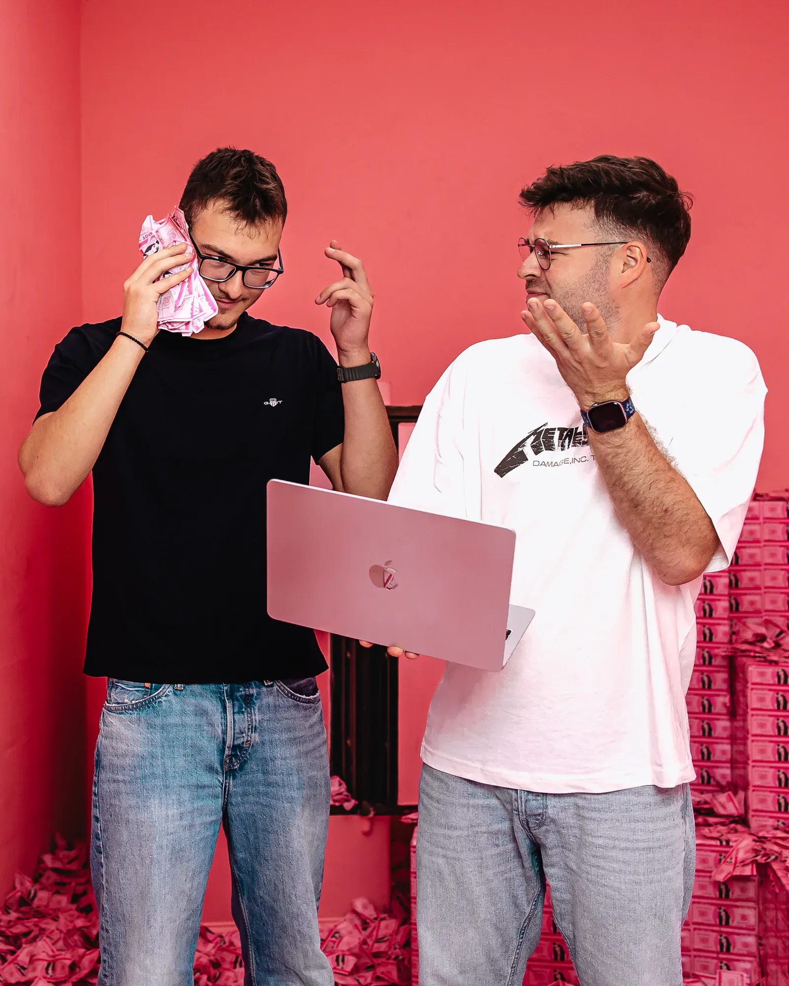 Zwei Webentwickler stehen mit pinkem Geld und einem Macbook in einem pinken Tresor