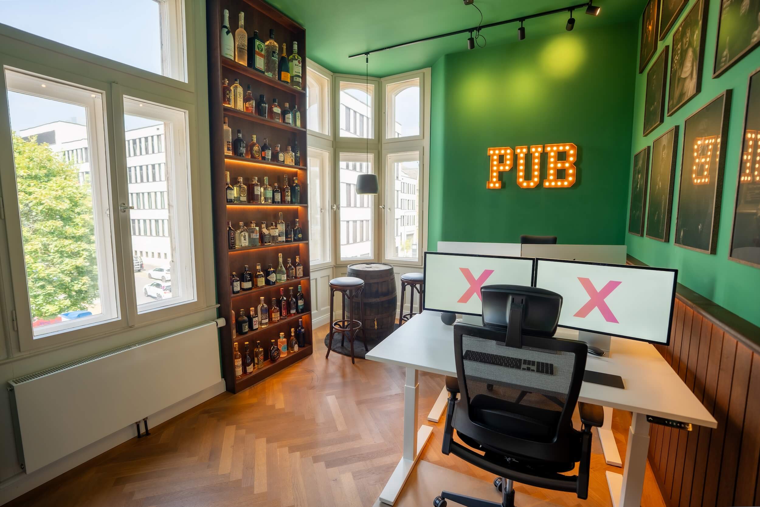 Arbeitsplatz im Exportarts Pub Büro mit Alkoholwand, grünen Wänden und beleuchtetem PUB Schriftzug
