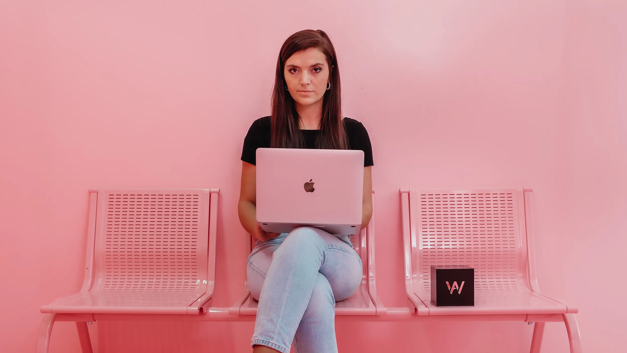 Social Media Expertin sitzt mit Macbook auf dem Schoß auf einer pinken Bank