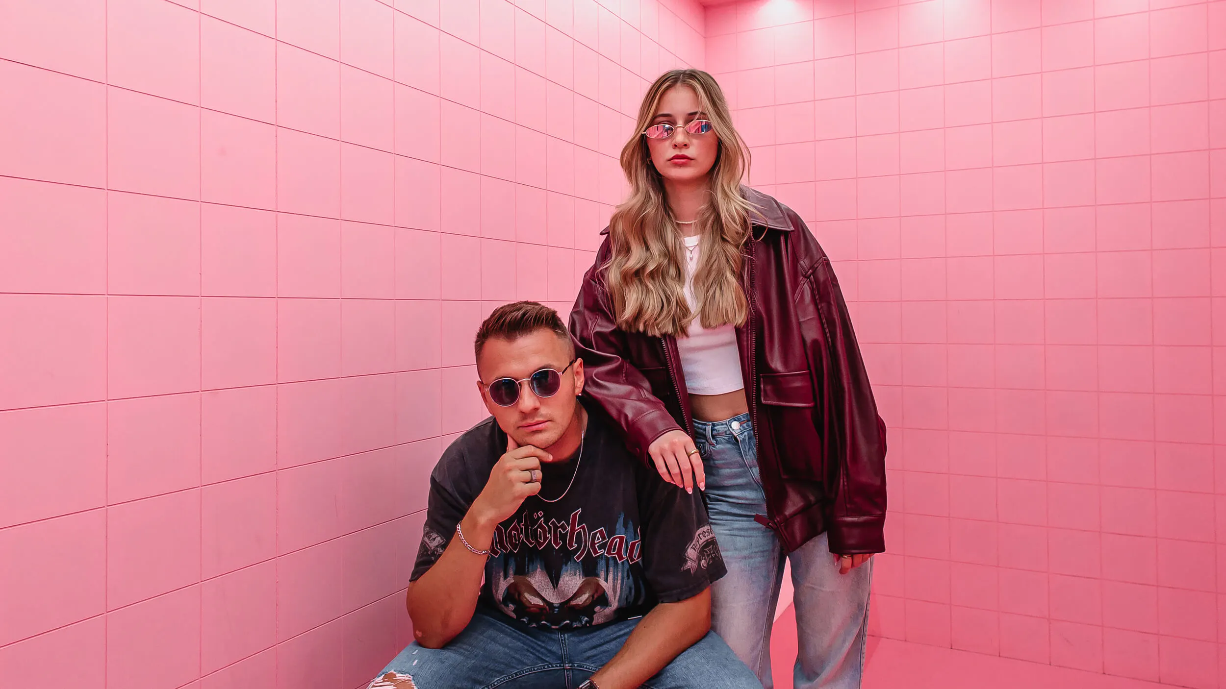 Zwei Mitarbeiter der Marketingagentur posieren vor einer pinken Wand