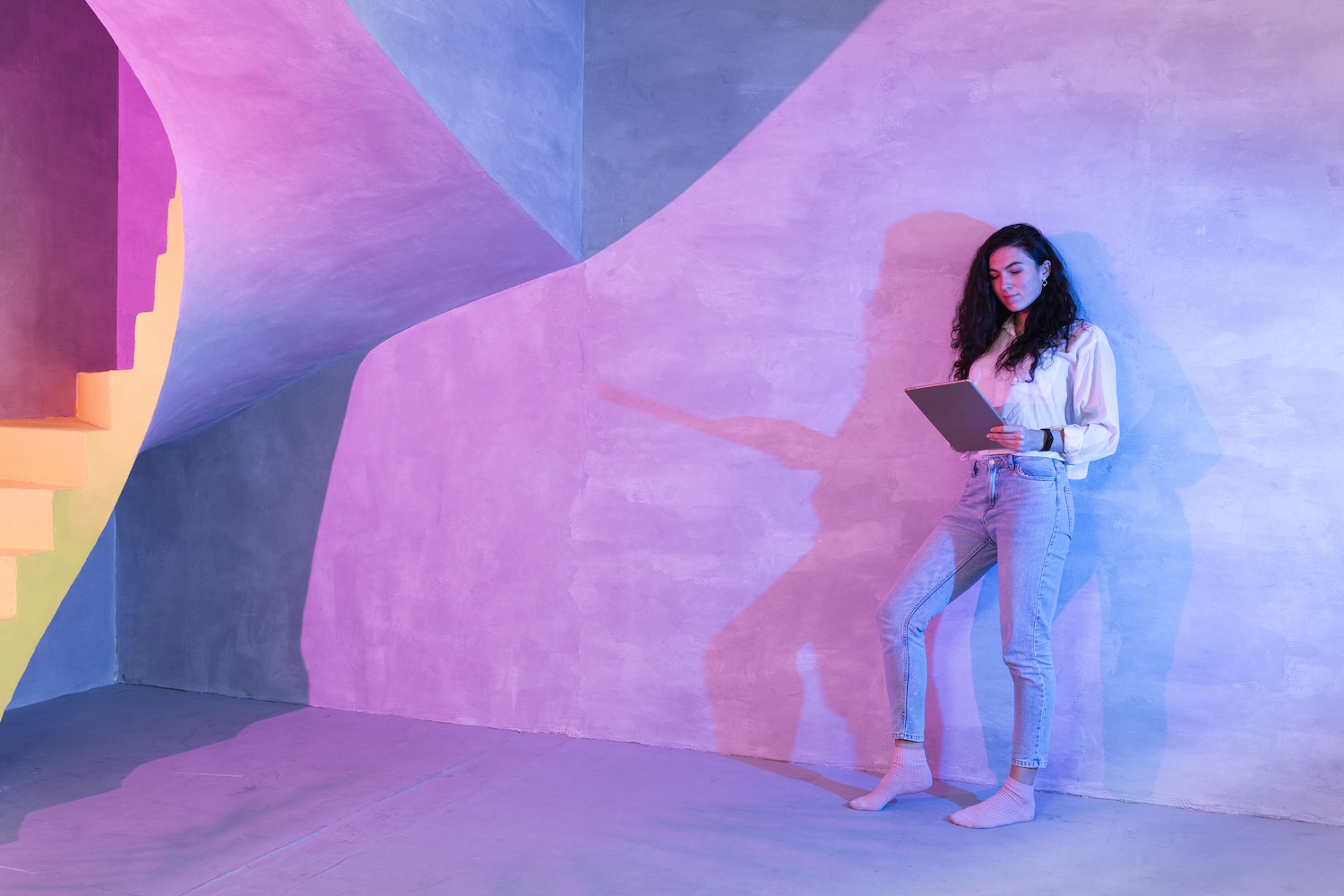 Frau mit Laptop lehnt sich an Wand