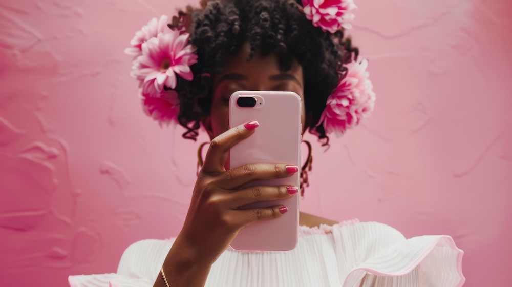Frau steht vor einer pinken Wand und hält Smartphone vor ihr Gesicht