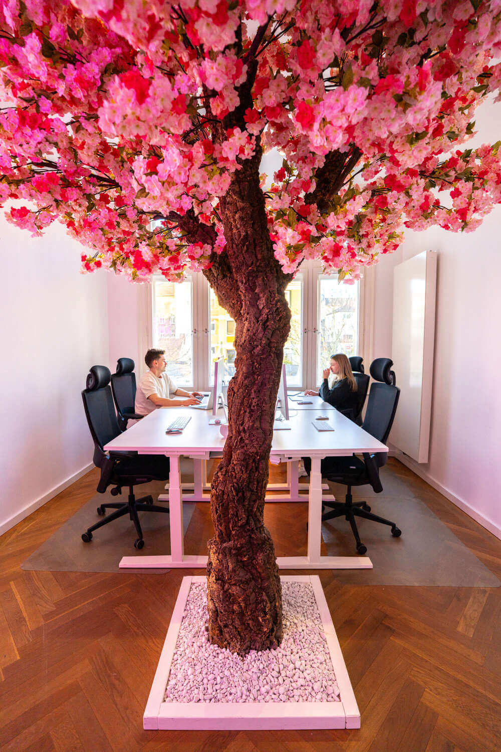 Büro im Exportarts Office mit großem Tisch und pinkem Kunstbaum als zentrales Element