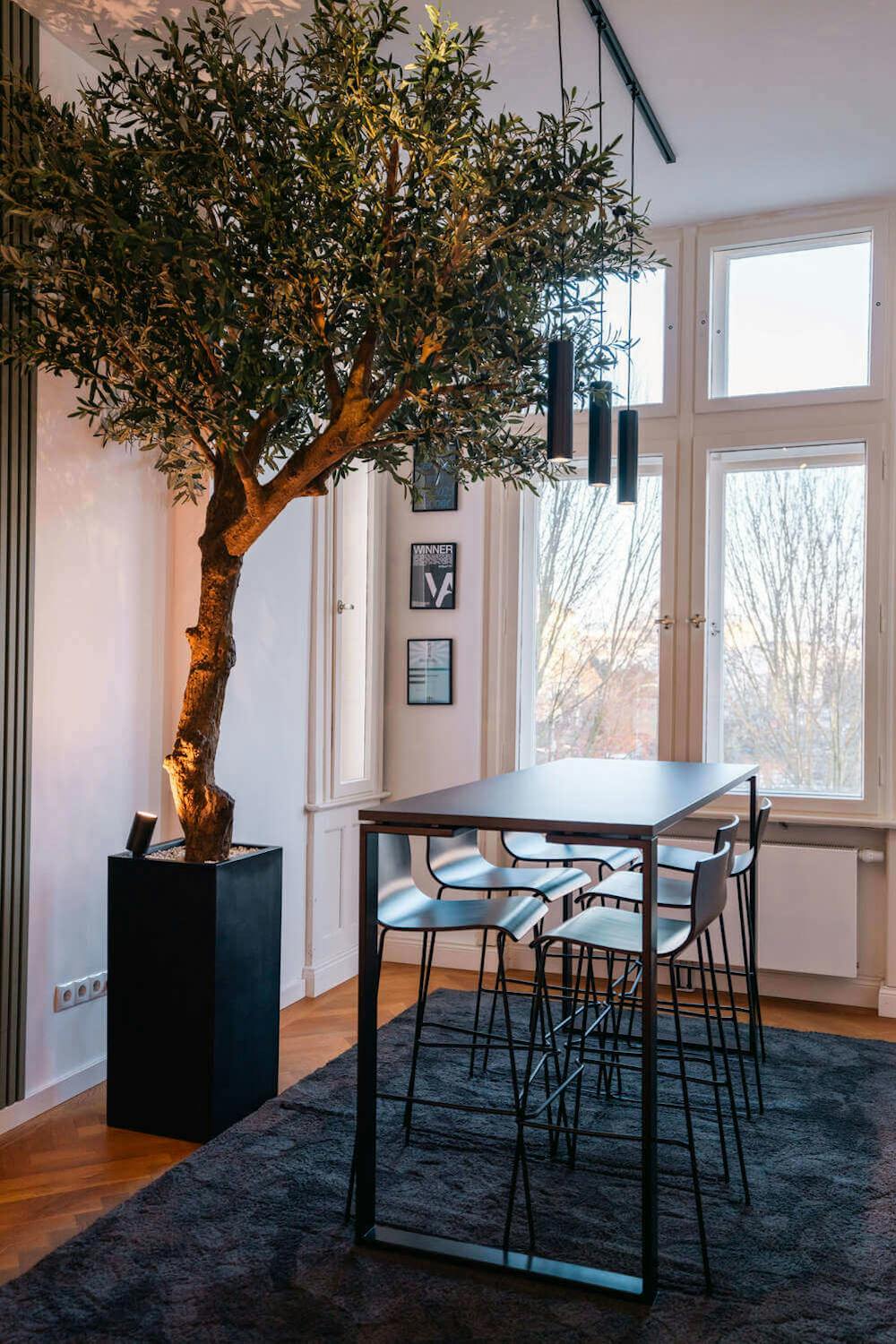 Meetingbereich im Exportarts Büro mit Stehtisch, Barhockern und dekorativem Baum Meetingbereich im Exportarts Büro mit Stehtisch, Barhockern und dekorativem Baum